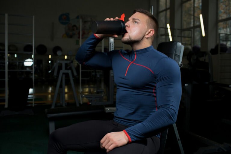 Homem ingerindo suplemento em shaker durante treino na academia, ilustrando o uso de suplementos para ganhar massa muscular.